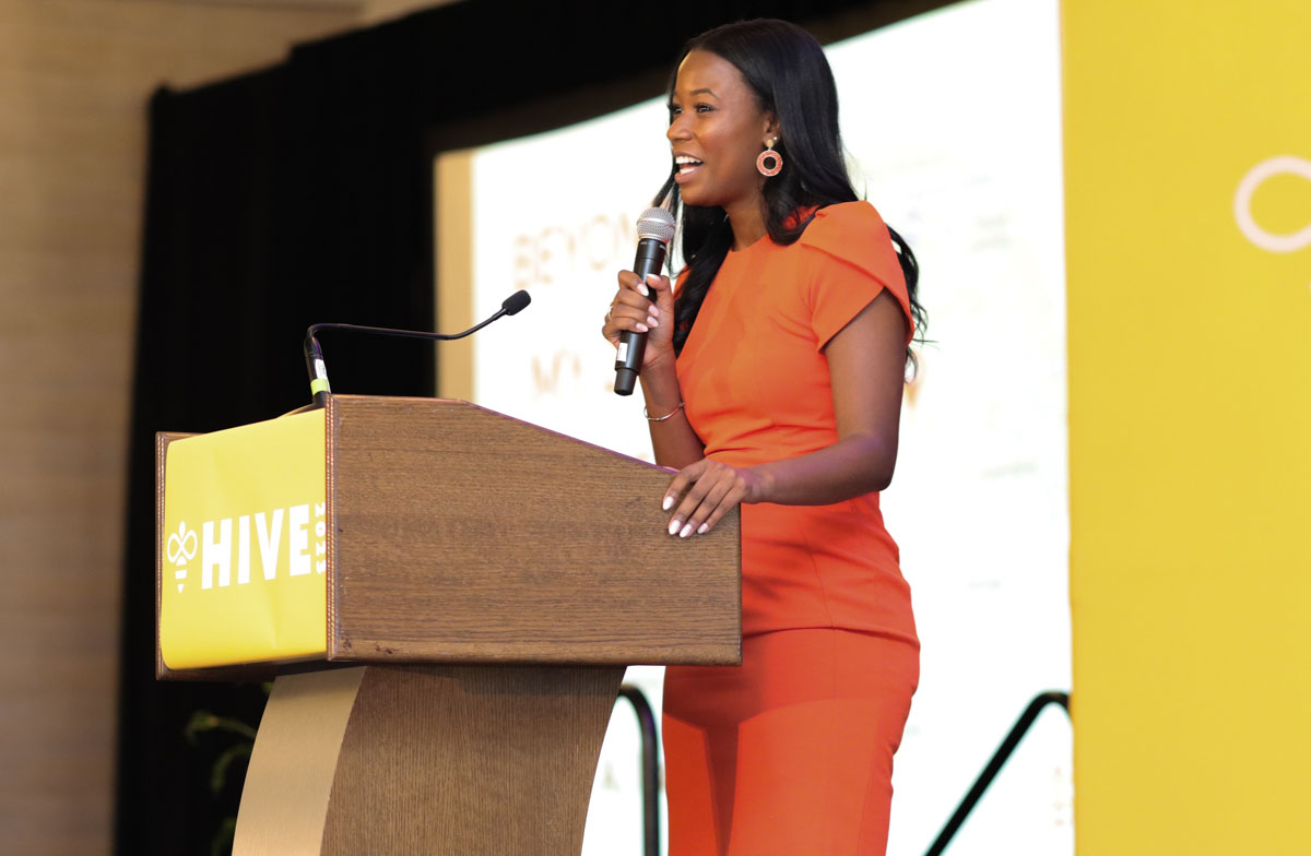 Iysha Dent standing at a podium speaking at Hive 2023